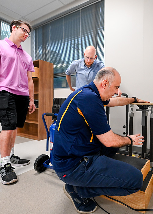 A man kneeling over equipment while two men watch.