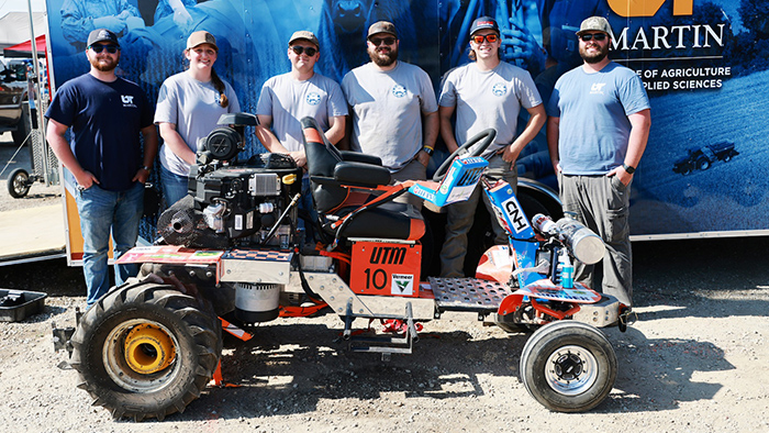 Six people posing for a photo with a custom built tractor.